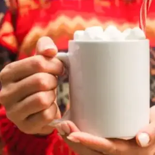 A woman holding a cup of hot cocoa wearing a christmas sweater.
